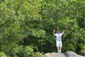 Man standing on rock in the forest showing a peace sign.