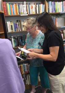 two women looking at sheet of paper in front of a bookshelf.