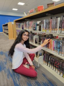 teen sitting and looking at books on library shelf