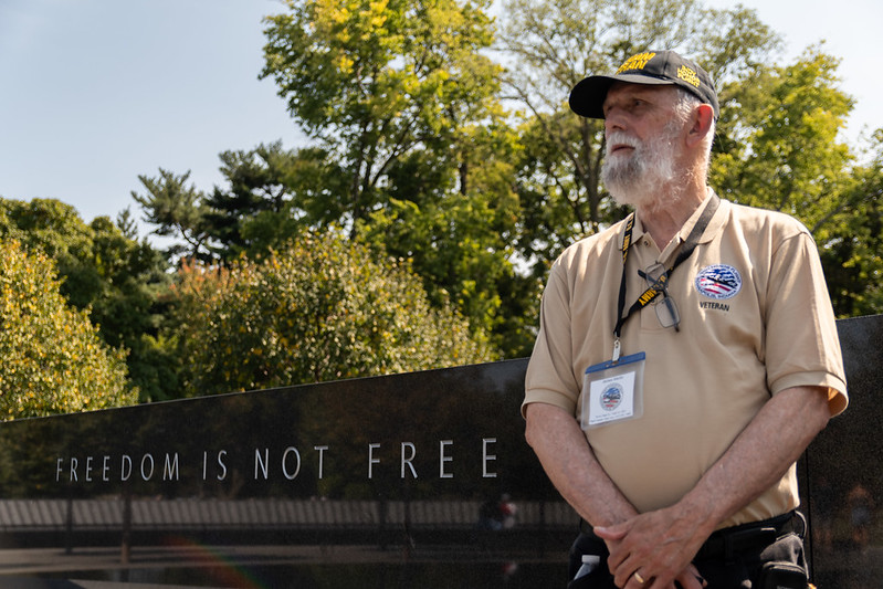 Veteran standing in front of war memorial that reads Freedom is not Free