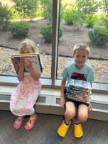 two kids smiling with stacks of books