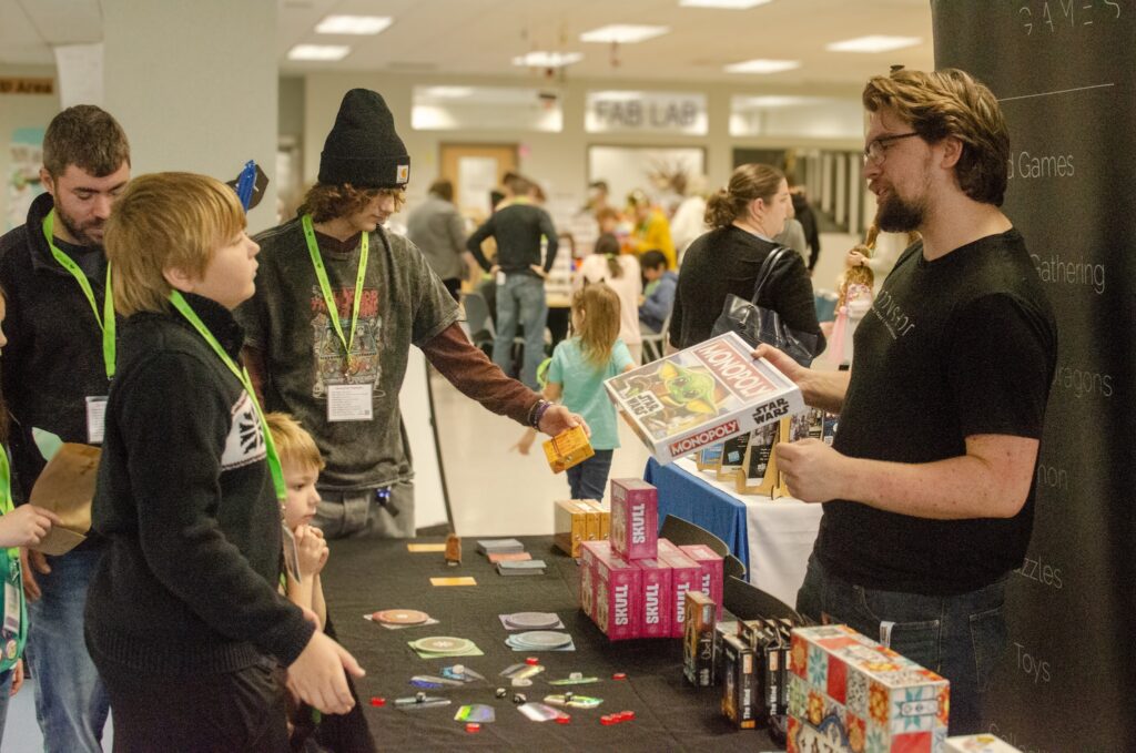 visitors talking to man at board game booth