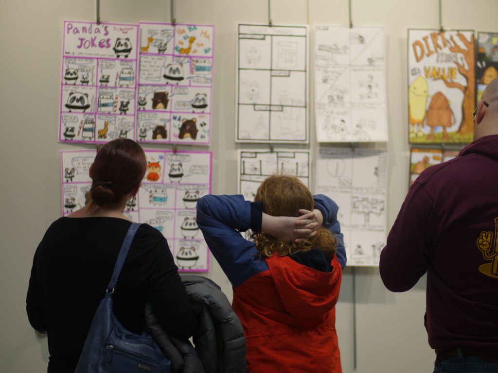people looking at pages from comics displayed in a gallery