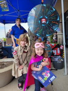 two children in front of a prize wheel dressed as a ghostbuster and superhero