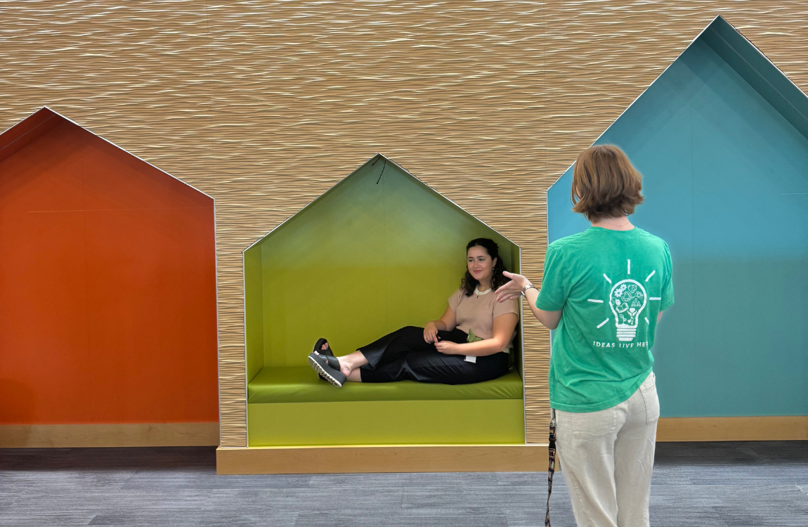two women talking by red green and blue house cutouts in the wall