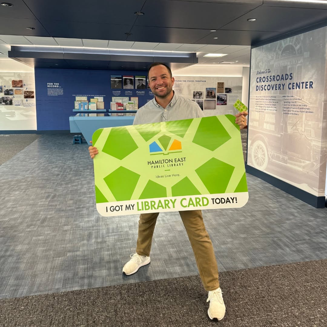 Man holding giant green library card that says 